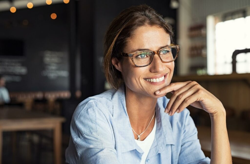 Smiling woman wearing stylish tortoiseshell eyeglasses indoors, highlighting modern eyewear styles and eyeglass fashion trends for 2026.