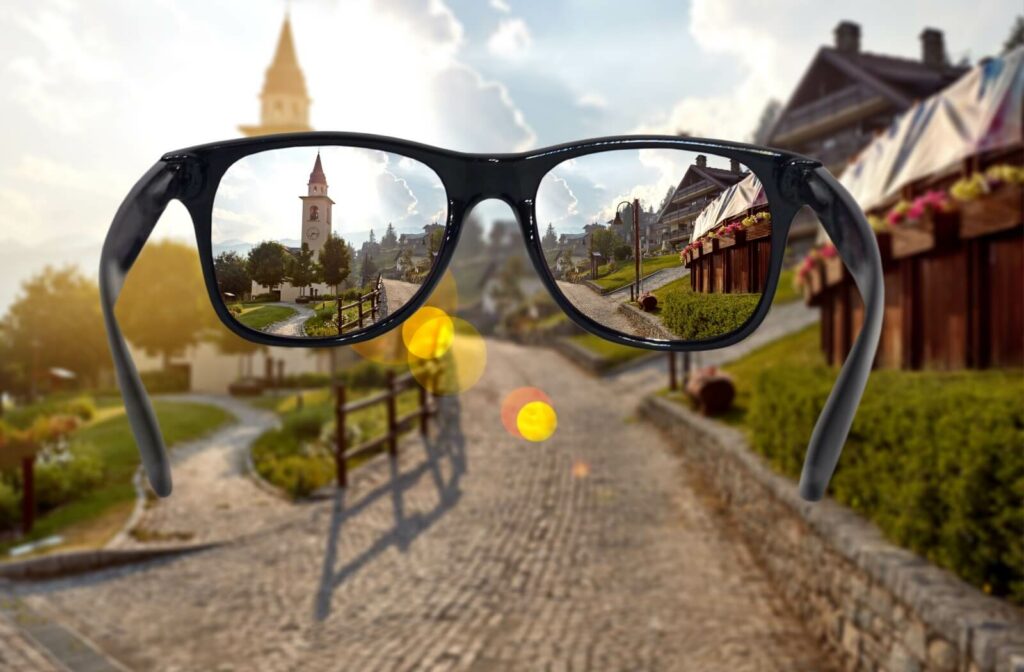 A view through glasses with anti-glare coating showing a crisp, clear landscape, compared to the blurry, sun-flared view outside the lenses.