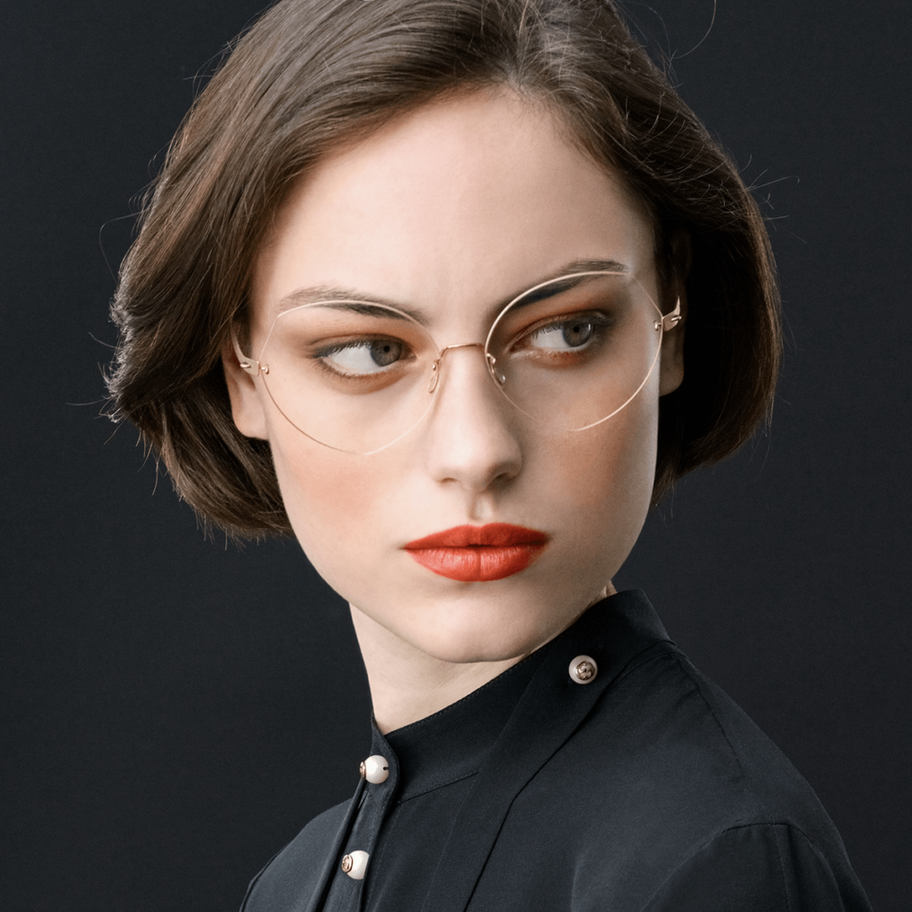 Woman wearing stylish round eyeglasses and a black blouse against a dark background.